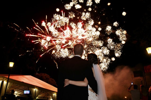 Happy hugging bride and groom watching beautiful colorful firewo